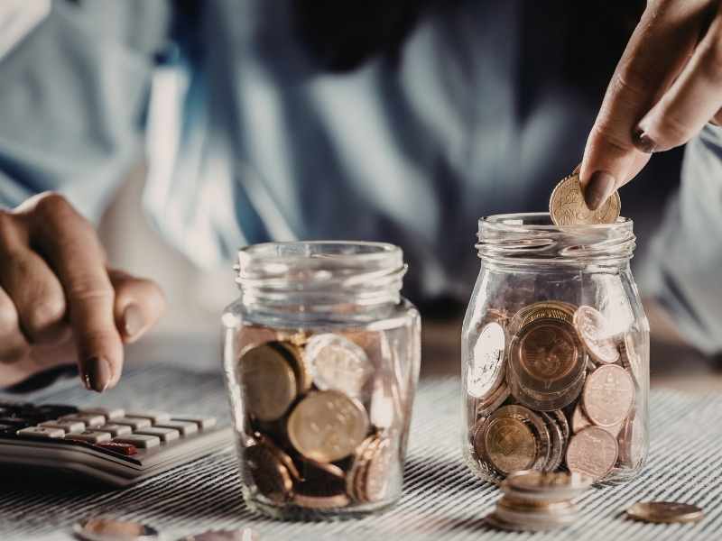 Frascos de vidrio con monedas sobre una mesa, representando ahorro y planificación de cuotas.