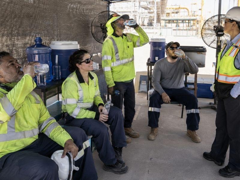 Trabajadores toman una pausa de hidratación en una zona con sombra, agua y ventilación para prevenir riesgos por altas temperaturas.