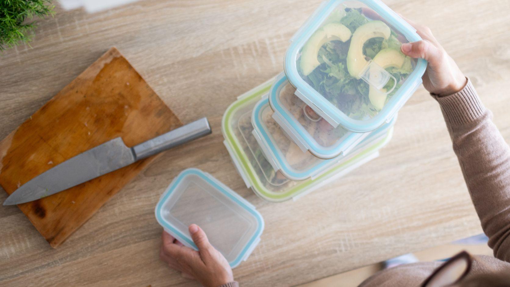 Recipientes con alimentos preparados y verduras sobre una mesa de cocina para organizar las comidas de la semana.