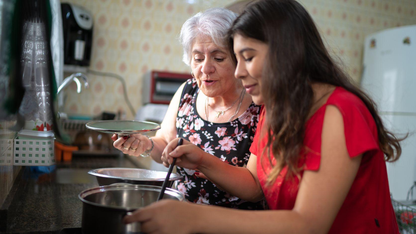 Abuela y nieta preparando una receta juntas en la cocina, como parte de la transmisión de tradiciones familiares.